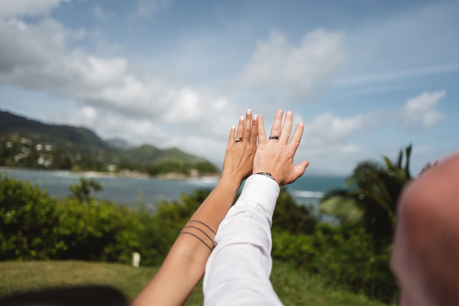 Bride and groom raising their ringed hands to the Seychelles sea and hills
